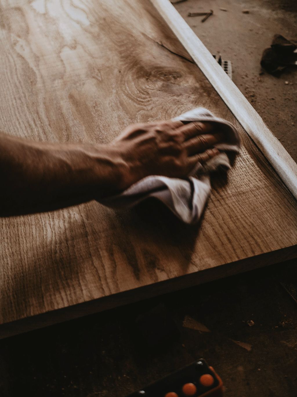 Eine Hand wischt mit einem Tuch Öl über eine Holzplatte, auf der Oberfläche glänzen Ölreste.