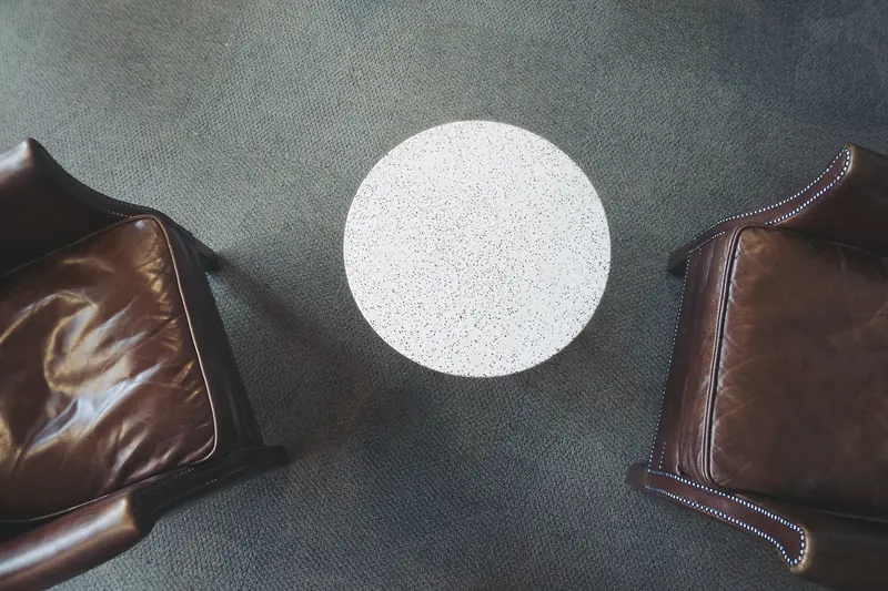 Zwei braune Ledersessel und ein kleiner runder Tisch auf grauem Teppich, von oben fotografiert.